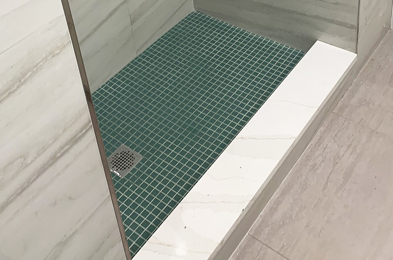 Open shower niche with triple shower system and green mosaic floor